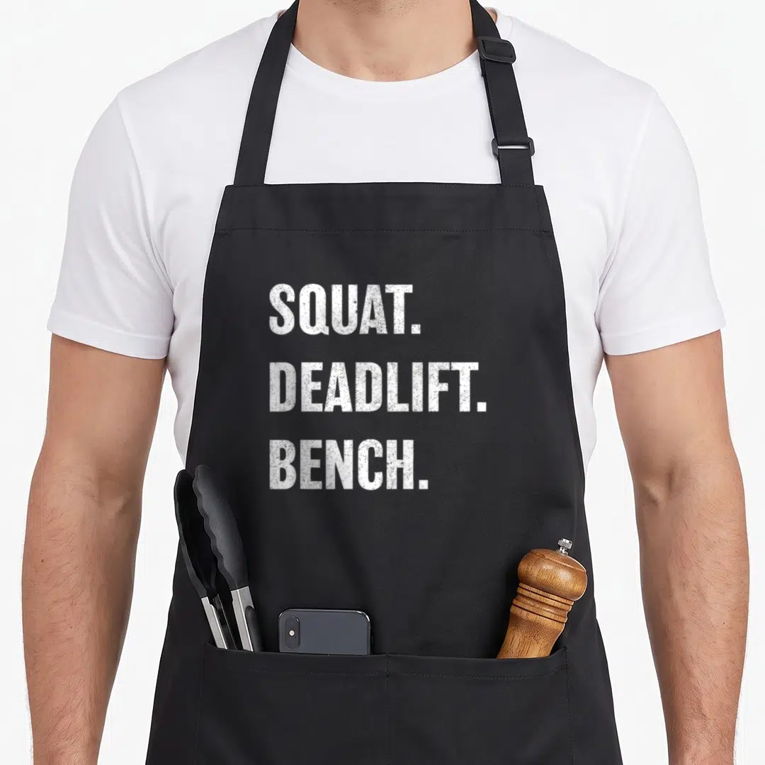 Weightlifting bench apron - White SQUAT. DEADLIFT. BENCH. stacked text on black background — shown on a black cotton canvas apron against a white background