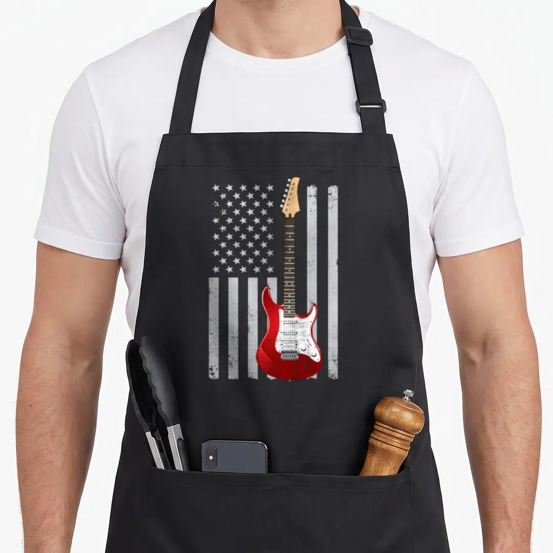 Funny guitar american flag apron - Red electric guitar overlaid on distressed white US flag stars and stripes — shown on a black cotton canvas apron against a white background