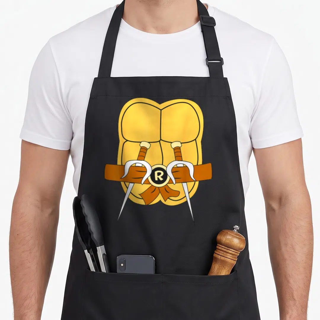 Raphael easy apron - Cartoon yellow stomach with brown belt two crossed swords R buckle — shown on a black cotton canvas apron against a white background