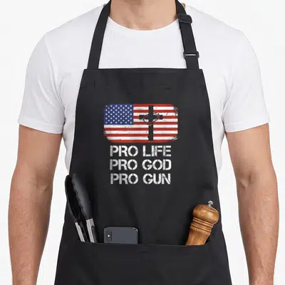Conservative gun apron - Distressed USA flag with grey cross white heart above three-line Pro Life Pro God Pro Gun text — shown on a black cotton canvas apron against a white background