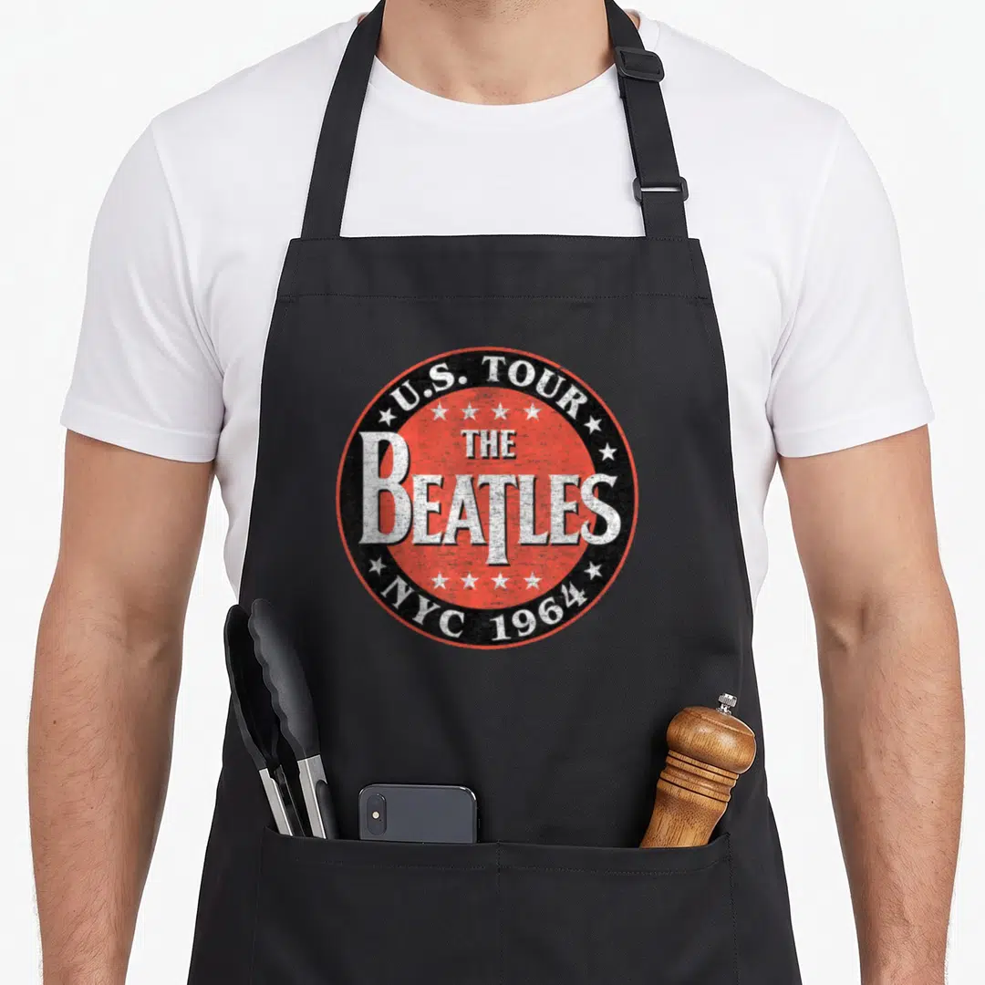 Tour nyc apron - Circular red and black logo with white stars and text U.S. TOUR THE BEATLES NYC 1964 — shown on a black cotton canvas apron against a white background