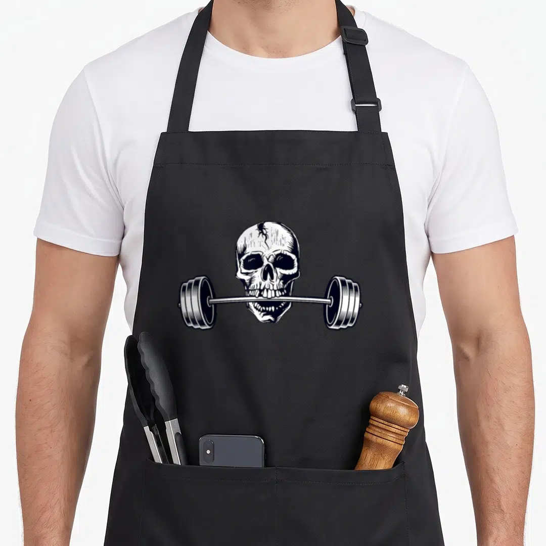 Weightlifting skull apron - White line art skull biting a barbell with weight plates on black background — shown on a black cotton canvas apron against a white background