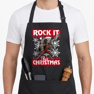Rocket christmas apron - Cartoon raccoon in santa hat holding gun with red knitted border and snowflakes — shown on a black cotton canvas apron against a white background