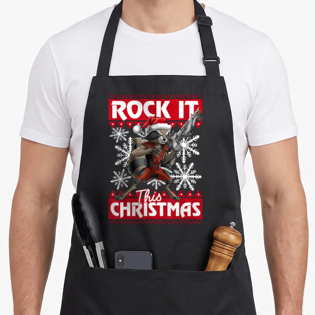 Rocket christmas apron - Cartoon raccoon in santa hat holding gun with red knitted border and snowflakes — shown on a black cotton canvas apron against a white background