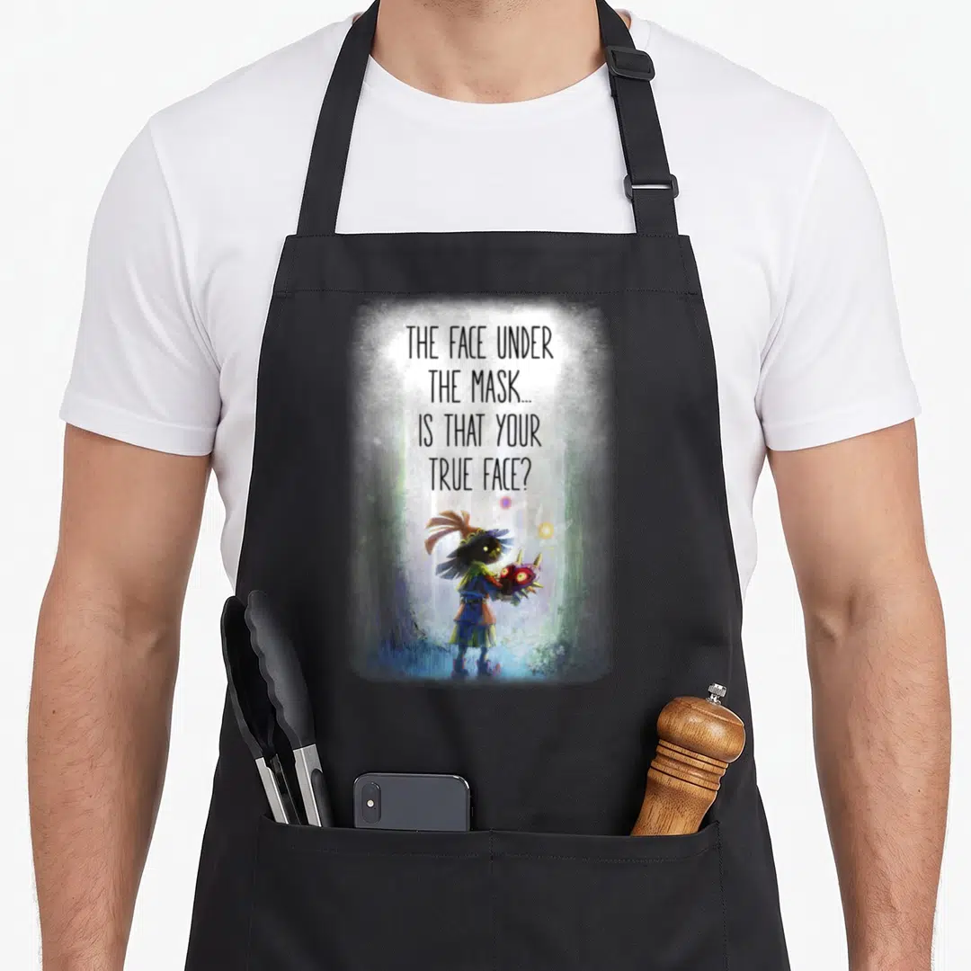 Majoras face apron - Character holding a mask in a forest under stacked text questioning true identity — shown on a black cotton canvas apron against a white background
