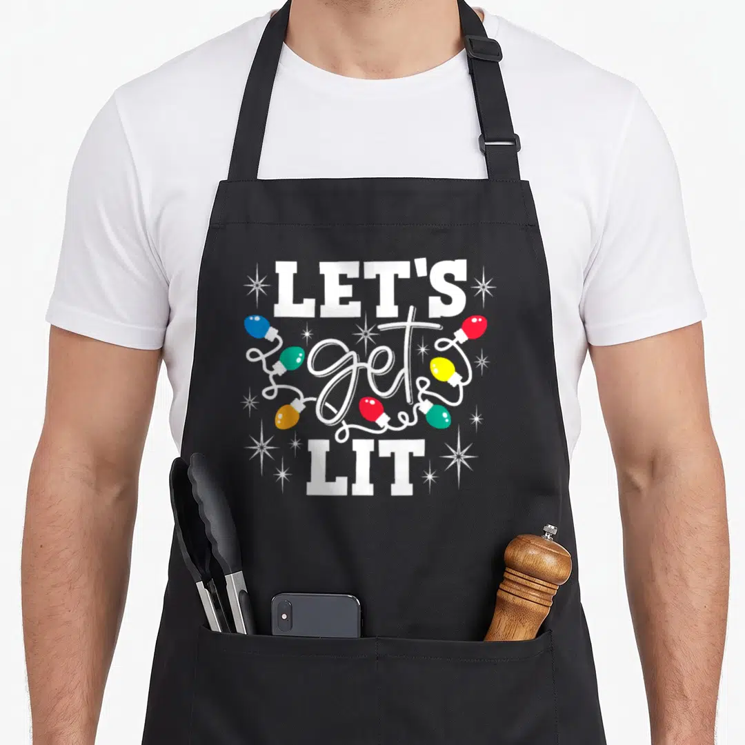 Lit santa aprons - LET'S get LIT text surrounded by colorful cartoon Christmas light bulbs and white sparkles — shown on a black cotton canvas apron against a white background