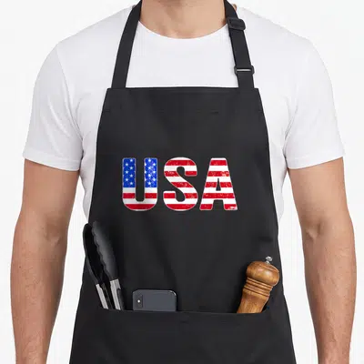 Vintage flag 4th of july apron - Distressed USA text filled with blue stars and red white stripes — shown on a black cotton canvas apron against a white background