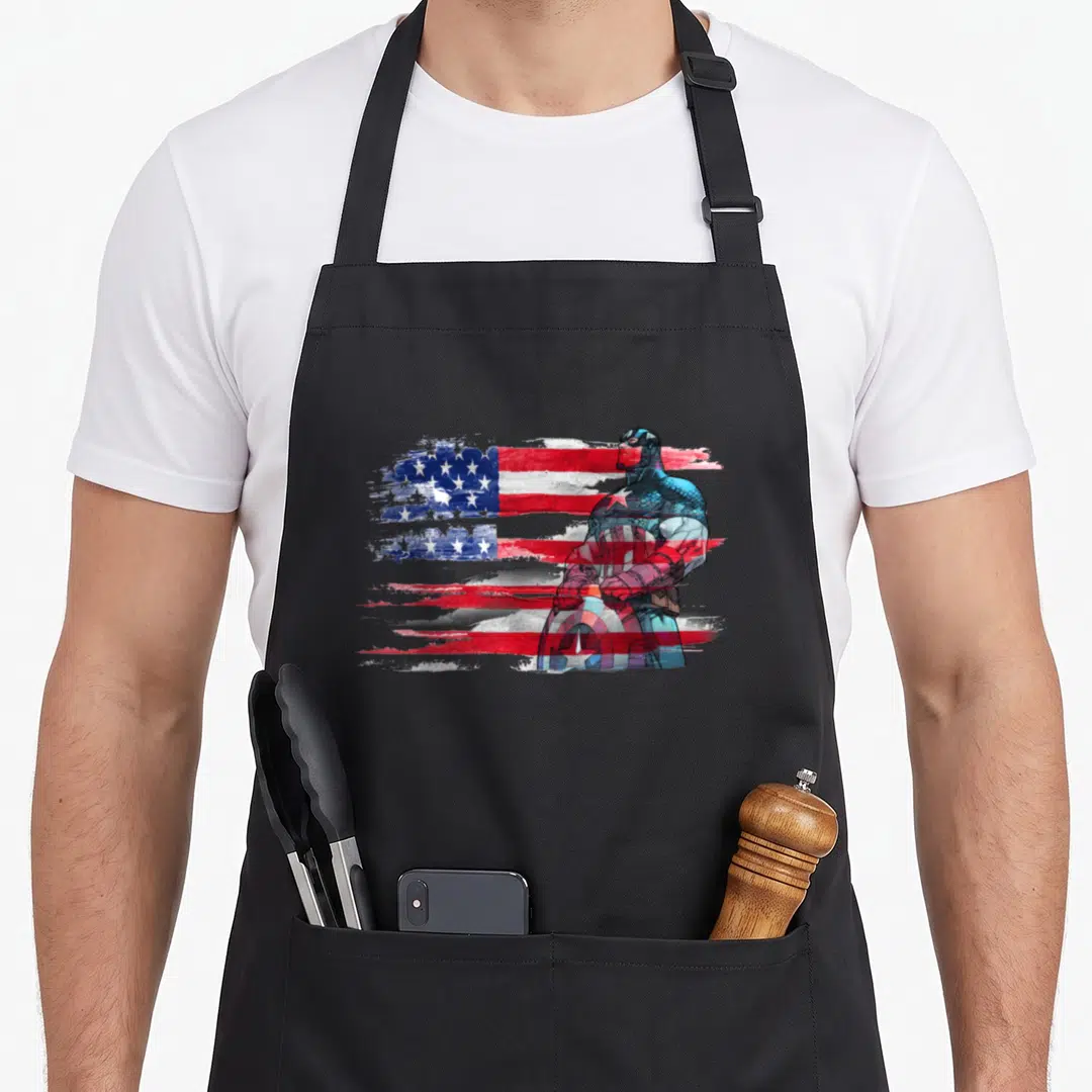 Stand captain apron - Captain America standing holding shield over distressed red white and blue American flag — shown on a black cotton canvas apron against a white background