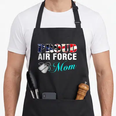 Proud air american flag apron - PROUD AIR FORCE Mom text with flag fill and two white dog tags — shown on a black cotton canvas apron against a white background