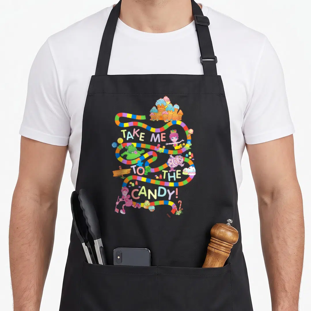 Funny land cotton candy apron - Multicolored winding path with TAKE ME TO THE CANDY text and cartoon sweets — shown on a black cotton canvas apron against a white background