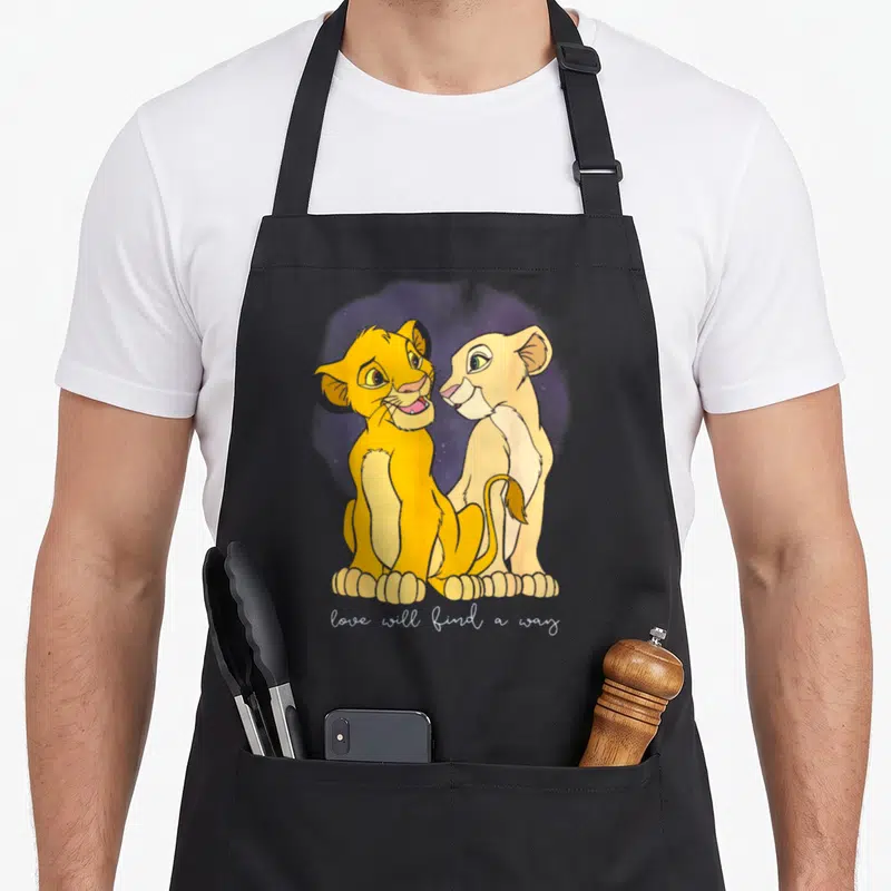 Simba valentine's day apron - Two yellow cartoon lion cubs sitting side by side under purple stars with white text — shown on a black cotton canvas apron against a white background