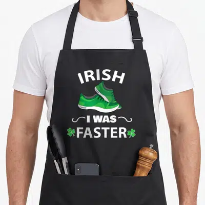 Faster st patrick day aprons - Two green sneakers below arched IRISH text and FASTER flanked by shamrocks — shown on a black cotton canvas apron against a white background