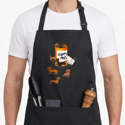 Funny pill dachshund apron - Orange pill bottle with happy pills text and seven cartoon dachshunds in black and tan — shown on a black cotton canvas apron against a white background