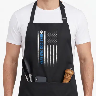 Flag dog apron - Vertical distressed US flag with blue BEST DOG DAD EVER text and white paw print — shown on a black cotton canvas apron against a white background