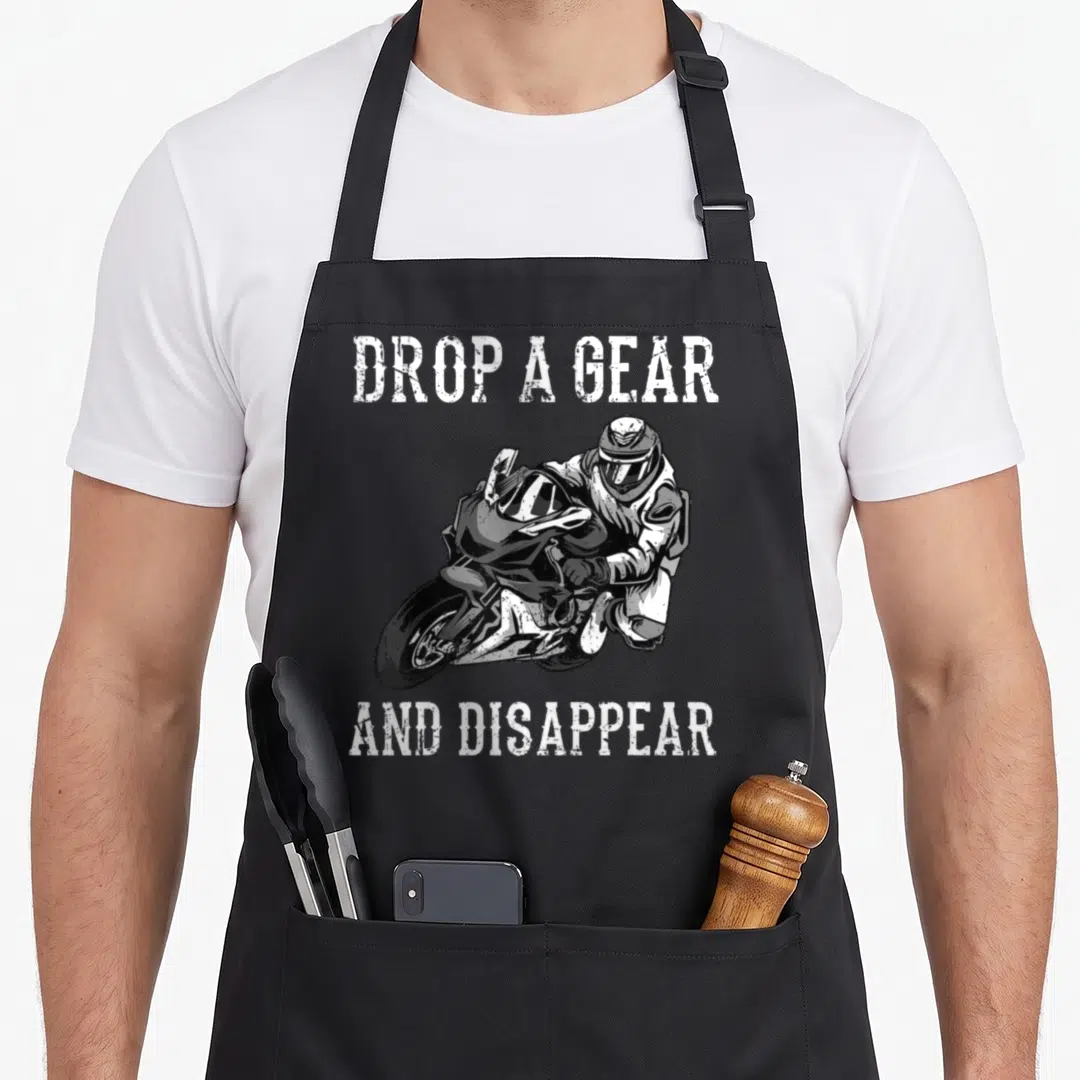 Rider motorbike motorcycle apron - Distressed text Drop A Gear And Disappear surrounding a black and white leaning — shown on a black cotton canvas apron against a white background