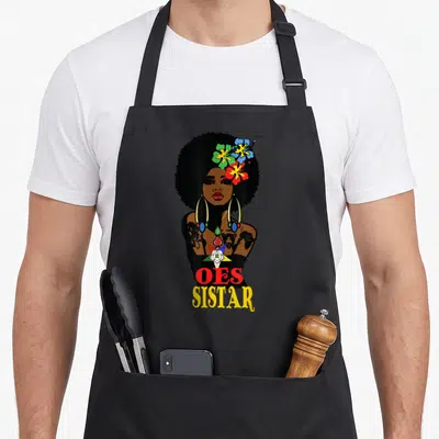 Diva oes apron - Cartoon woman with afro, flowers, star emblem, and OES SISTAR text — shown on a black cotton canvas apron against a white background
