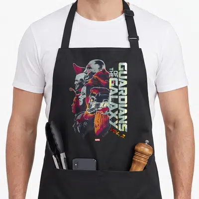 Epic galaxies apron - Guardians of the Galaxy Vol 2 vertical text with overlapping character faces in yellow red blue — shown on a black cotton canvas apron against a white background