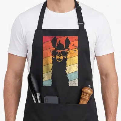 Llama alpaca apron - Grey llama silhouette with sunglasses over red orange yellow blue retro stripes — shown on a black cotton canvas apron against a white background
