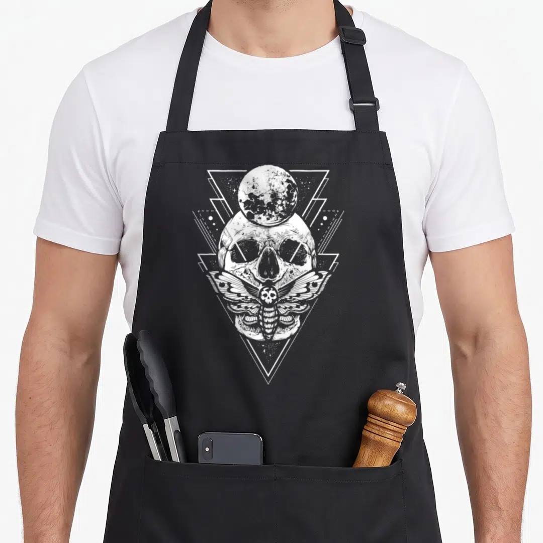 Crystal skeleton apron - White line art skull, moth, and moon inside a geometric downward triangle design — shown on a black cotton canvas apron against a white background