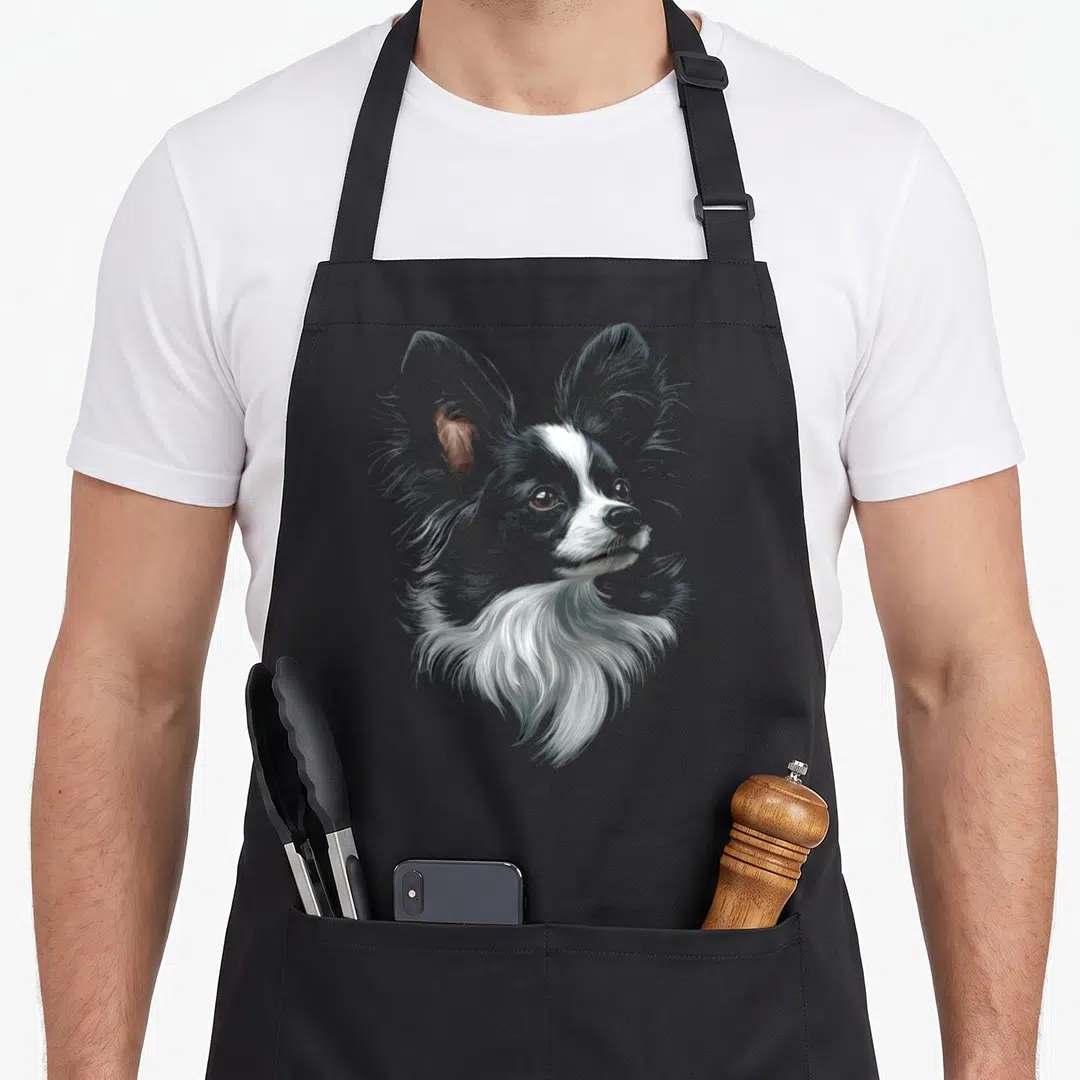Papillon motif dog apron - Realistic grey white and brown illustration of a Papillon dog head centered on an apron — shown on a black cotton canvas apron against a white background
