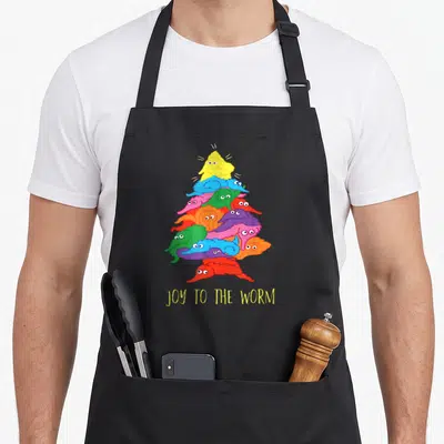 Joy christmas tree apron - Stack of colorful cartoon worms in triangle shape with text JOY TO THE WORM below — shown on a black cotton canvas apron against a white background