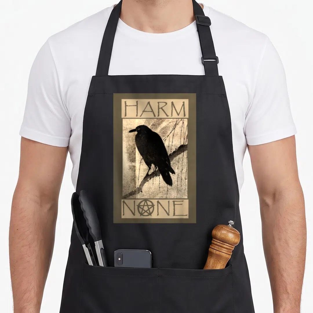 Harm wiccan apron - Black crow on branch with Harm None text and pentacle in olive and beige — shown on a black cotton canvas apron against a white background