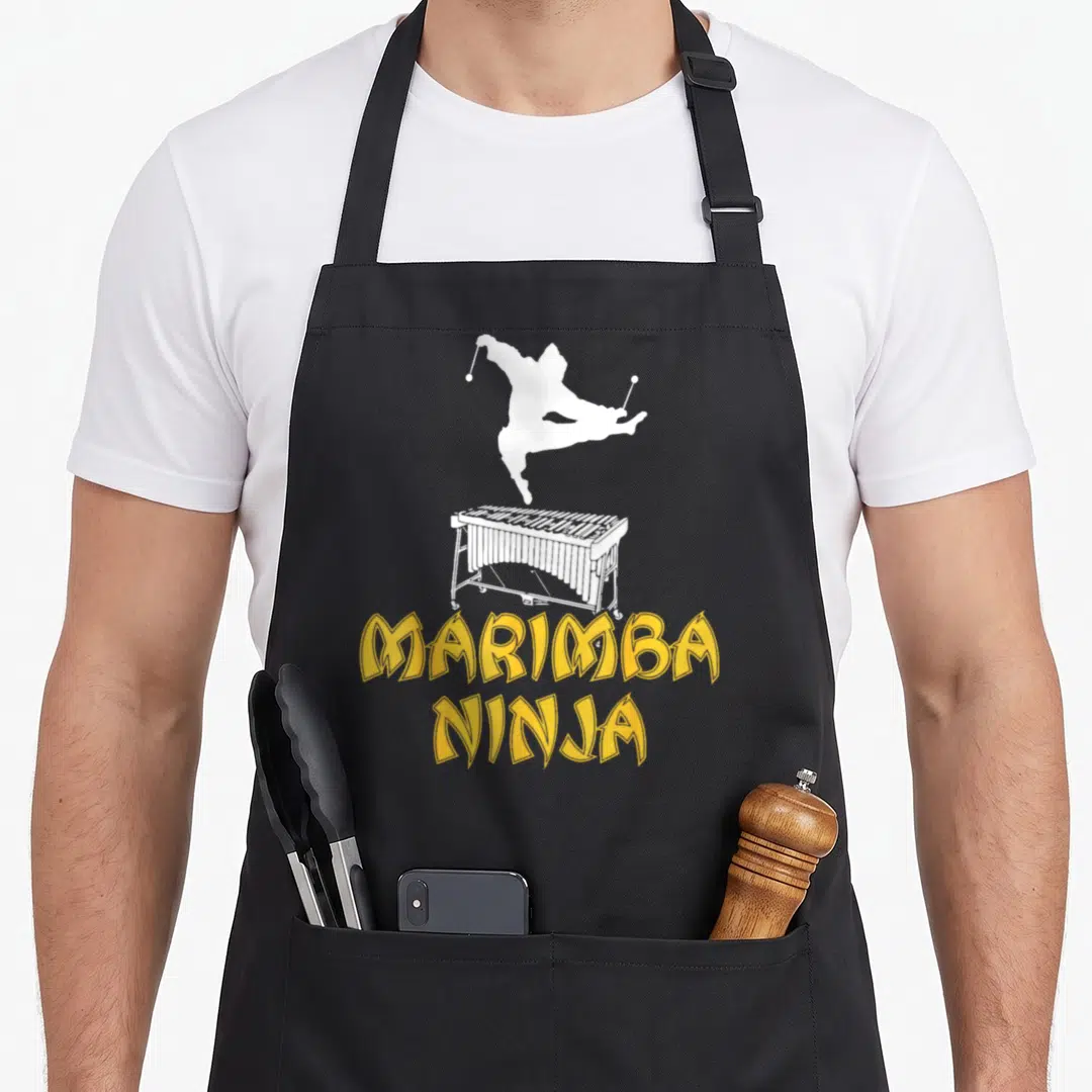 Marimba crew apron - White ninja jumping over marimba with yellow MARIMBA NINJA text — shown on a black cotton canvas apron against a white background
