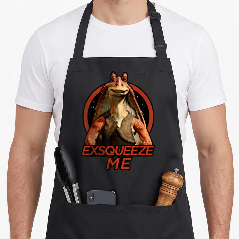 Jar star apron - Alien centered in orange circle with EXSQUEEQUEEZE ME text below — shown on a black cotton canvas apron against a white background