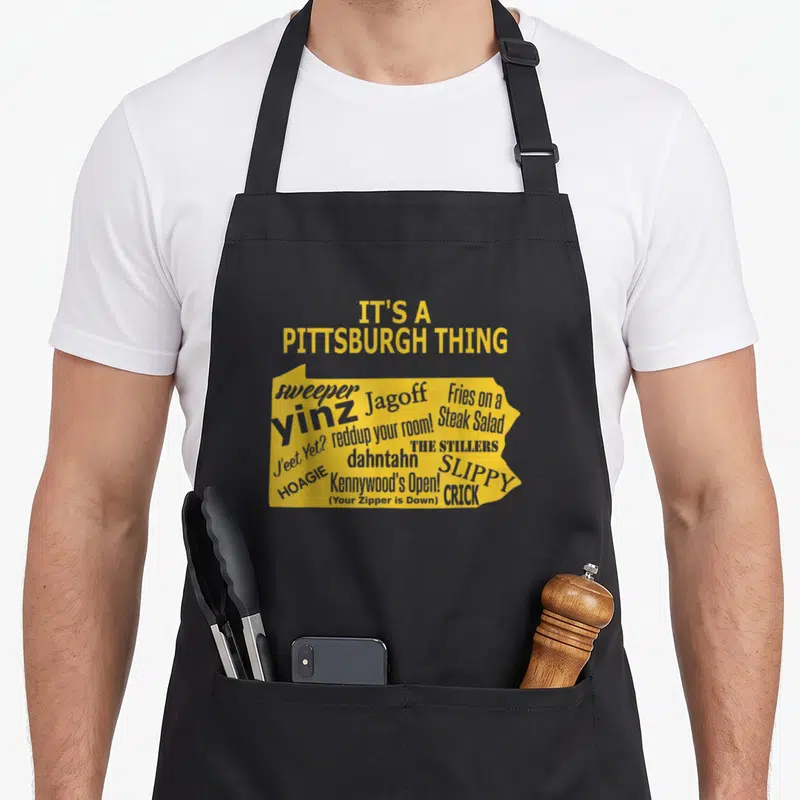 Funny yinzer pittsburgh men women kids apron - Yellow PA map silhouette filled with grey Pittsburgh slang text — shown on a black cotton canvas apron against a white background