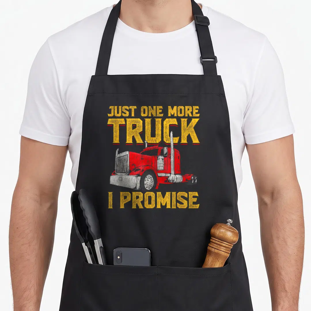 Papa truck apron - Red and white truck illustration with distressed yellow text Just One More Truck I Promise — shown on a black cotton canvas apron against a white background