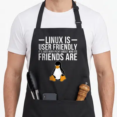 Linux friends apron - White text above a black and orange cartoon penguin with an angry expression — shown on a black cotton canvas apron against a white background