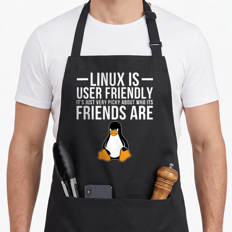 Linux friends apron - White text above a black and orange cartoon penguin with an angry expression — shown on a black cotton canvas apron against a white background