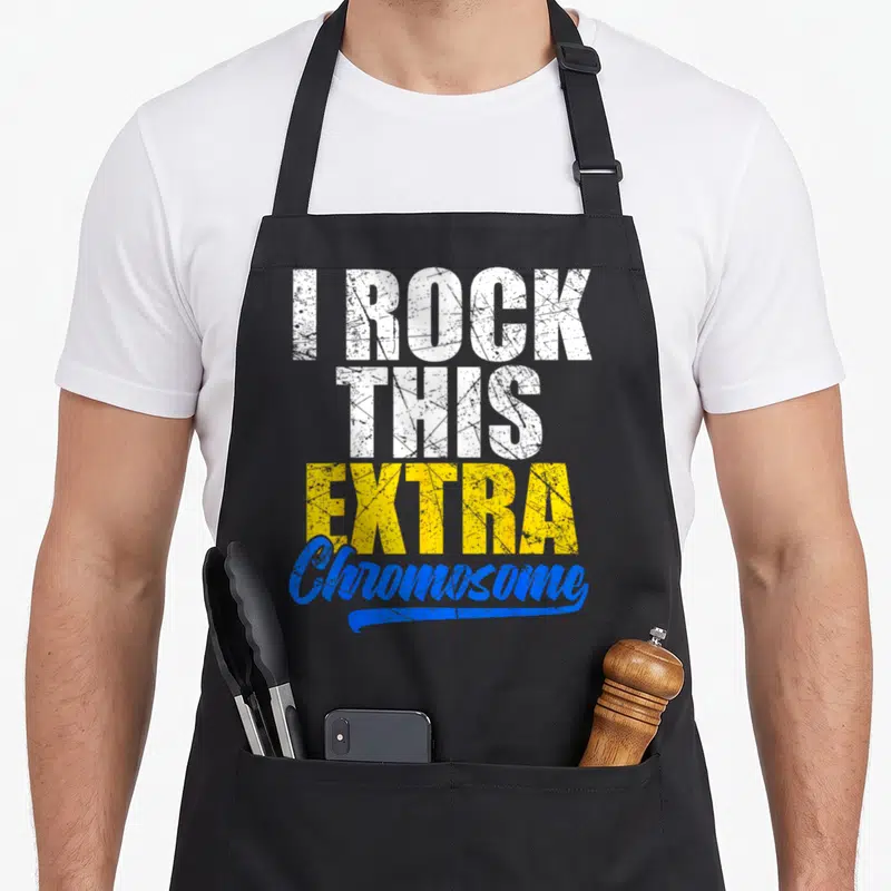 Rock an extra apron - Stacked distressed text I ROCK THIS EXTRA Chromosome in white yellow and blue — shown on a black cotton canvas apron against a white background