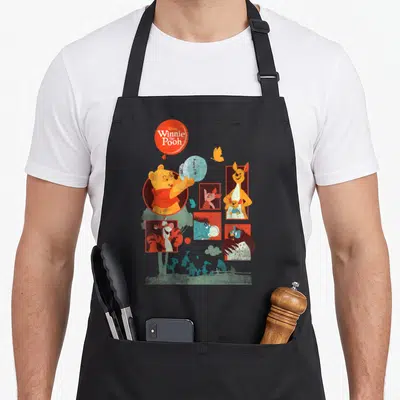 Panel friends apron - Winnie the Pooh holds blue HUNNY balloon surrounded by friends in red frames with teal silhouettes — shown on a black cotton canvas apron against a white background