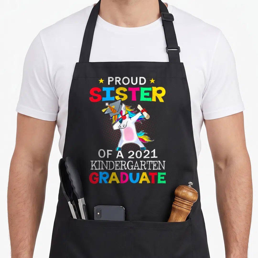 Sister unicorn aprons - Cartoon white unicorn dabbing with cap and scroll flanked by colorful proud sister graduate text — shown on a black cotton canvas apron against a white background