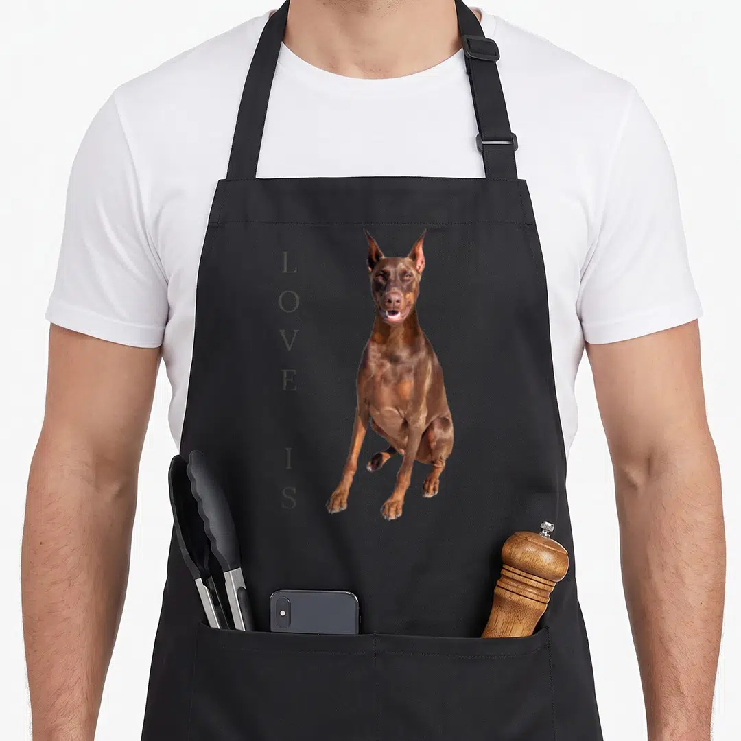 Pinscher pet dog apron - Vertical LOVE IS text beside a seated brown dog photo on grey background — shown on a black cotton canvas apron against a white background