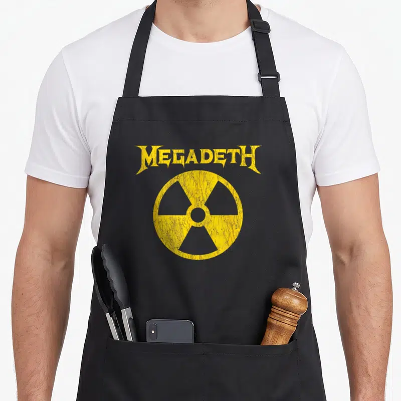 Nuclear heavy metal apron - Yellow MEGADETH text above cracked radiation symbol on grey background — shown on a black cotton canvas apron against a white background