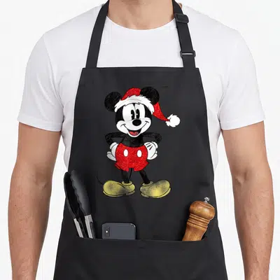 Cute christmas apron - Mickey Mouse cartoon wearing red Santa hat and shorts with yellow shoes — shown on a black cotton canvas apron against a white background