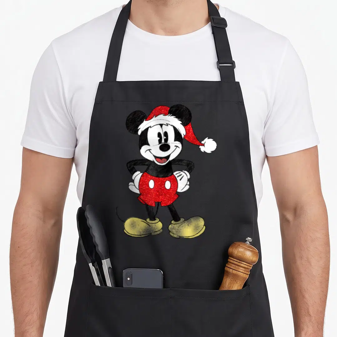 Cute christmas apron - Mickey Mouse cartoon wearing red Santa hat and shorts with yellow shoes — shown on a black cotton canvas apron against a white background