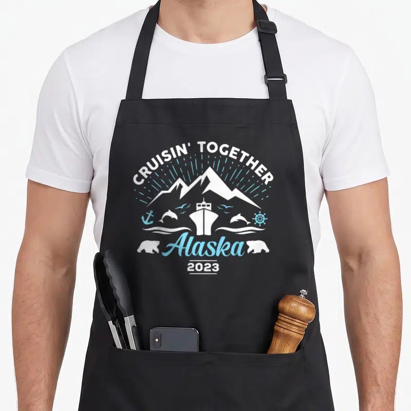 Alaska friends cooking apron - Cruisin Together Alaska 2023 cruise ship mountains dolphins bears anchor wheel — shown on a black cotton canvas apron against a white background