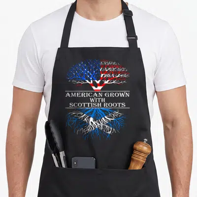 Grown scottish american apron - Tree with US flag canopy and Scottish saltire roots separated by text AMERICAN GROWN — shown on a black cotton canvas apron against a white background