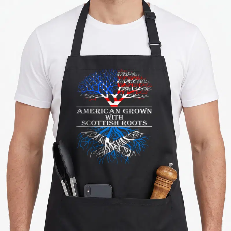 Grown scottish american apron - Tree with US flag canopy and Scottish saltire roots separated by text AMERICAN GROWN — shown on a black cotton canvas apron against a white background