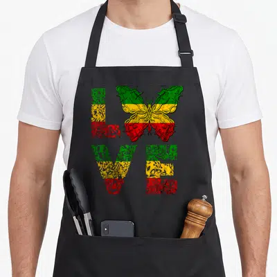 Reggae butterfly apron - LOVE text with butterfly replacing O, green yellow red bands, barbed wire outline — shown on a black cotton canvas apron against a white background