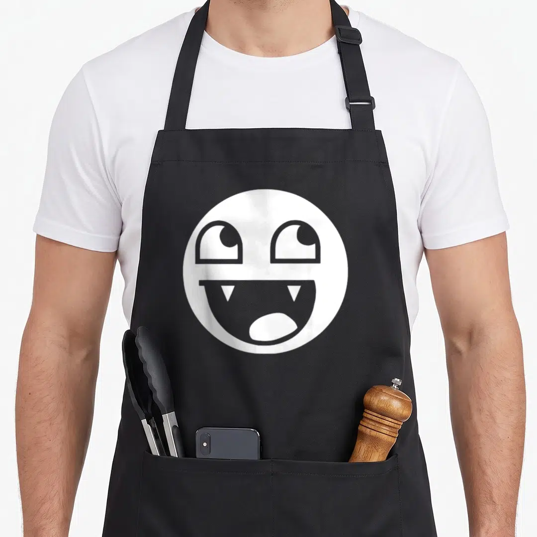 Epic streetwear apron - White circular smiley face with large eyes and fanged open mouth — shown on a black cotton canvas apron against a white background