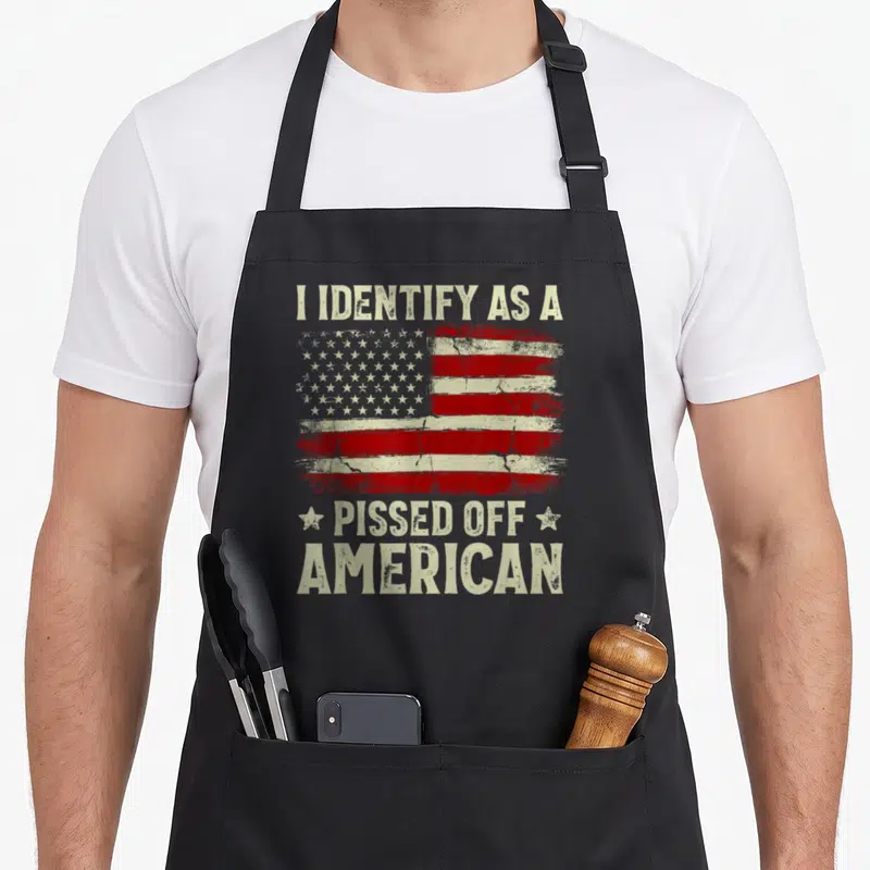 Pissed american flag apron - Distressed USA flag with I IDENTIFY AS A PISSED OFF AMERICAN text and two stars — shown on a black cotton canvas apron against a white background