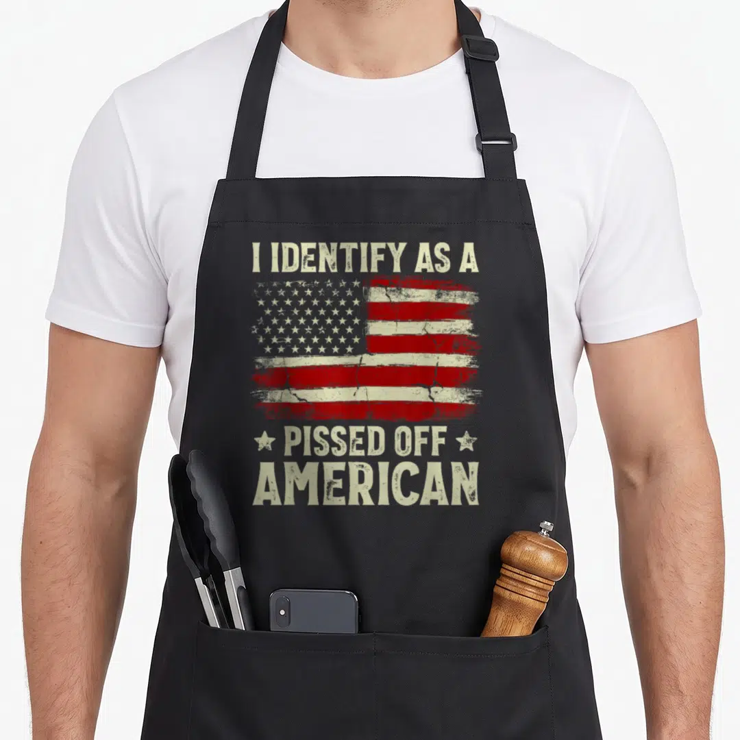 Pissed american flag apron - Distressed USA flag with I IDENTIFY AS A PISSED OFF AMERICAN text and two stars — shown on a black cotton canvas apron against a white background