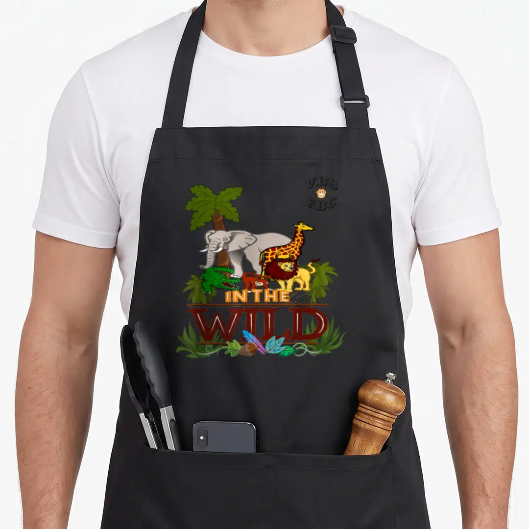 Wild theme aprons - Cartoon elephant, giraffe, lion, monkey, and crocodile under palm tree with In The Wild text — shown on a black cotton canvas apron against a white background