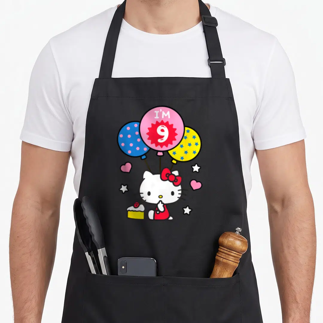 Cute hello general birthday apron - Hello Kitty holding three balloons with I'M 9 text and a cake slice — shown on a black cotton canvas apron against a white background