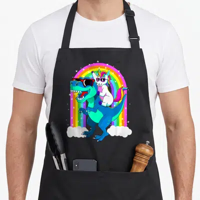 Trex dinosaur apron - Cartoon T-Rex and unicorn under rainbow with sunglasses and stars — shown on a black cotton canvas apron against a white background