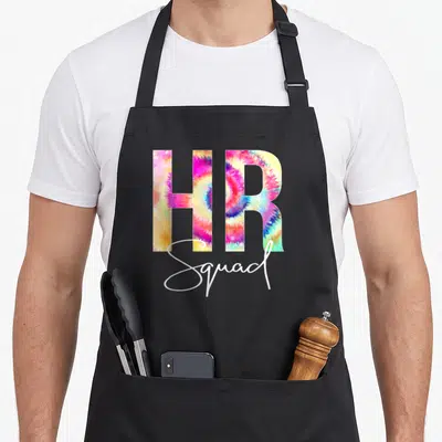 Squad tie-dye apron - HR Squad tie-dye text in pink yellow blue and white on black background — shown on a black cotton canvas apron against a white background